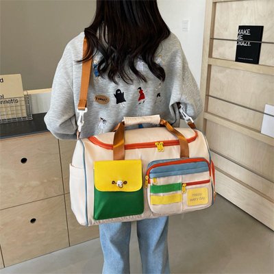 Femme de dos avec sac voyage crÚme multipoches colore poignées Camel tenue décontractée intérieur moderne style pratique quotidien