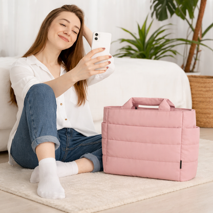 Femme assise au sol en visioconférence dans sa chambre d’hôtel, avec à ses côtés un sac de voyage cabine rose.