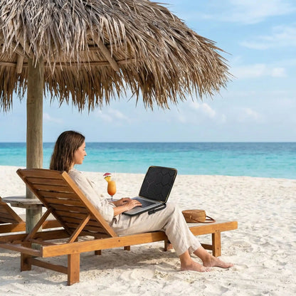 Femme travaillant sur la plage sous un parasol, utilisant une Pochette ordinateur Matelassée Voyage Zen noir pour protéger son PC portable en bord de mer.