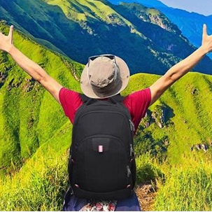 Homme portant le sac à dos de voyage, parfait pour la cabine, face à un paysage vert, les bras ouverts