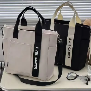 Petit sac week‑end femme blanc crème et noir sur table moderne, avec stores en arrière‑plan, style épuré et élégant