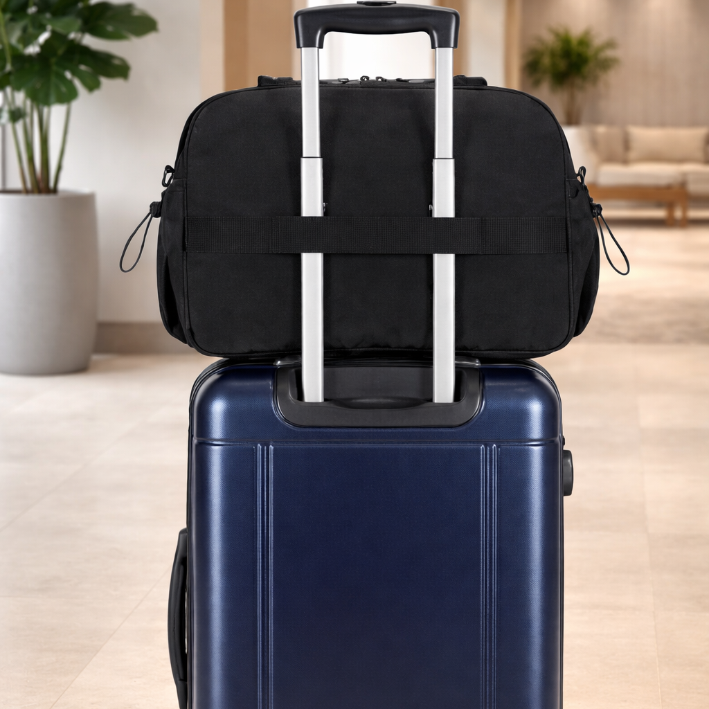 Valise bleu marine avec un sac noir fixé sur sa poignée télescopique. L'ensemble est posé dans un hall d'hôtel moderne, lumineux et épuré avec plantes.