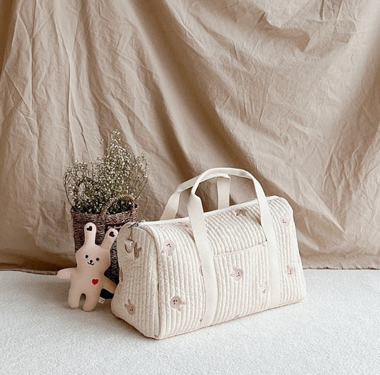 Trois sacs week end parfait pour bebe en coton matelasse poses cote a cote sur une étagère en bois clair avec petit toutou et plante