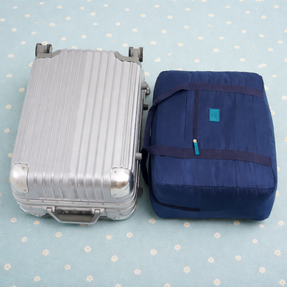 Sac de voyage bleu tibétain compact, idéal en bagage cabine, vu de côté près d’une petite valise trolley posée sur un lit
