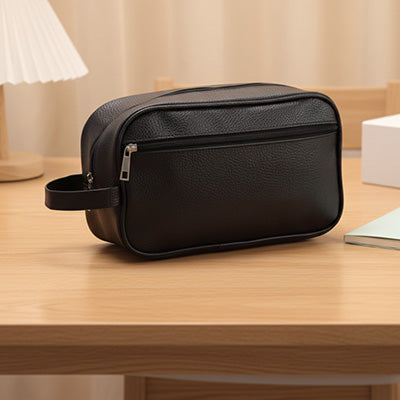 Trousse de toilette homme effet cuir noir, posée sur une petite table d’hôtel, lumière douce et ambiance zen