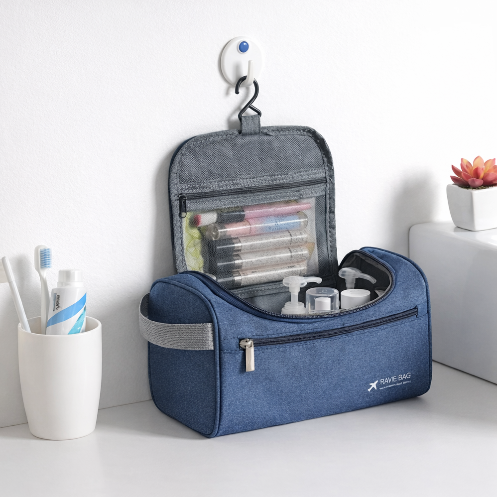 Trousse de voyage bleue suspendue au mur, ouverte avec compartiments visibles, contenant flacons, maquillage et accessoires de toilette dans une salle de bain.
