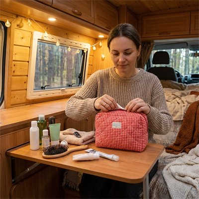 Dans une vanlife, une femme range essentiels dans une trousse de toilette rouge à carreaux