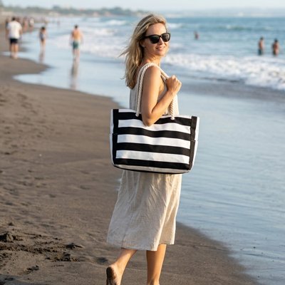 Femme à la plage en promenade au soleil avec sac de plage à rayures noir et blanc