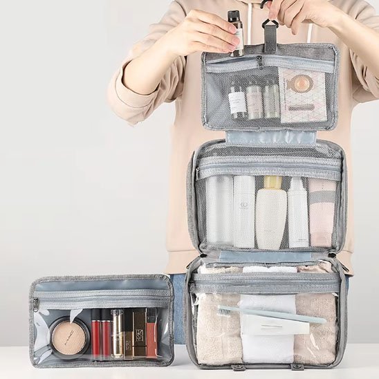 Femme soulève par le crochet robuste la trousse de toilette femme grise avec sa grande capacité de rangement