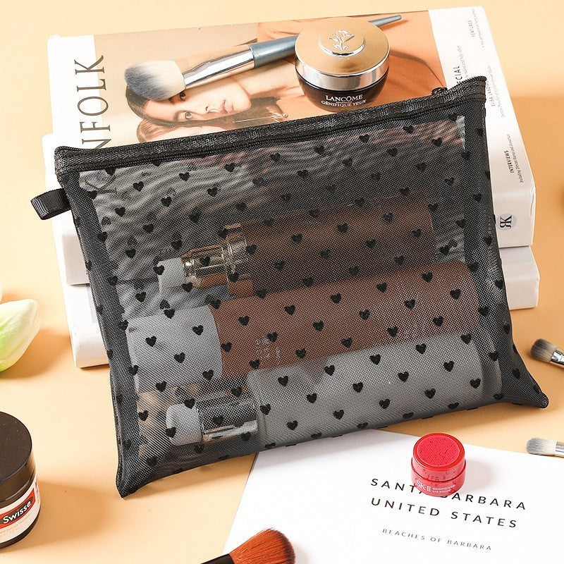 Grande pochette de maquillage noire, posée sur une table de nuit en bois