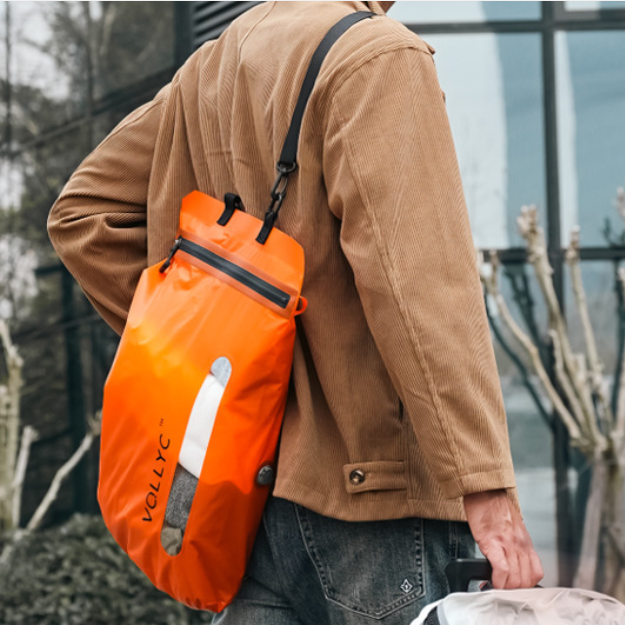 homme en milieu urbain portant en bandoulière le sac sous vide de voyage orange, format compact et étanche
