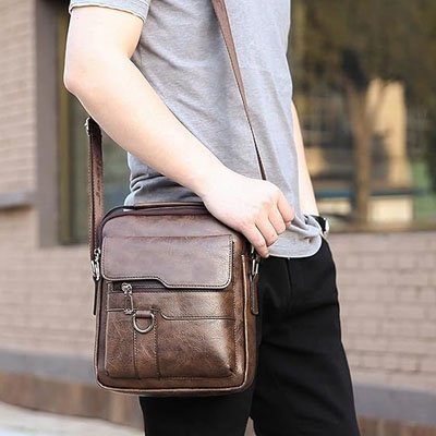 Homme porte un sac bandoulière homme en cuir marron à l’épaule, pratique et discret, idéal pour transporter ses essentiels en ville.