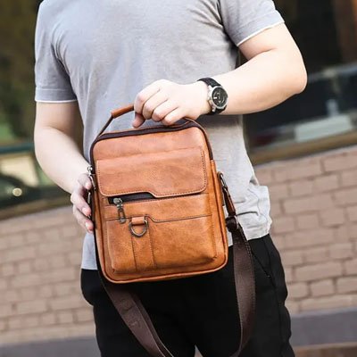 Homme tient un sac bandoulière homme en cuir marron, pratique et élégant, idéal pour transporter ses essentiels lors de ses déplacements.