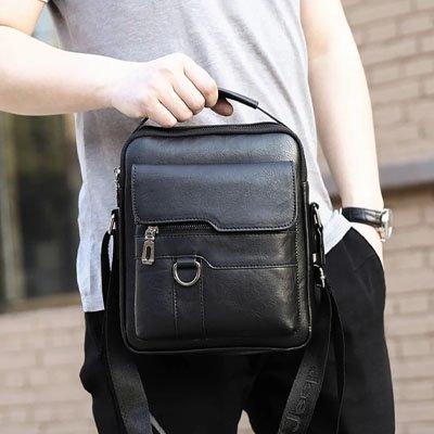 Homme tient un sac bandoulière homme noir en cuir, compact et élégant, idéal pour transporter ses essentiels avec style au quotidien
