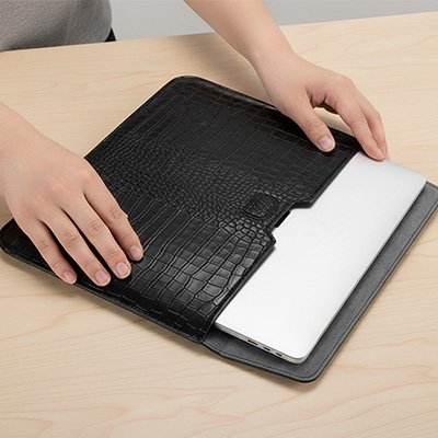 Housse pour ordinateur élégante en cuir texturé noir, avec ordinateur portable partiellement inséré sur un bureau clair