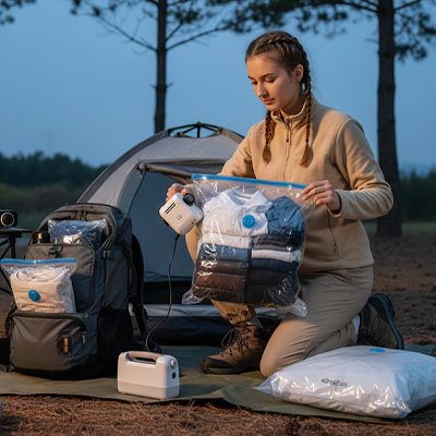 Jeune femme prépare sac sous vide pour voyage avec pompe électrique en bivouac, rangement compact de couvertures et vêtements