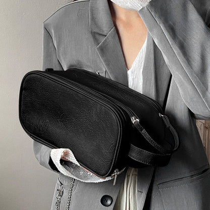 organisateur de maquillage noir porté à la main contre une veste grise vue proche matière texturée