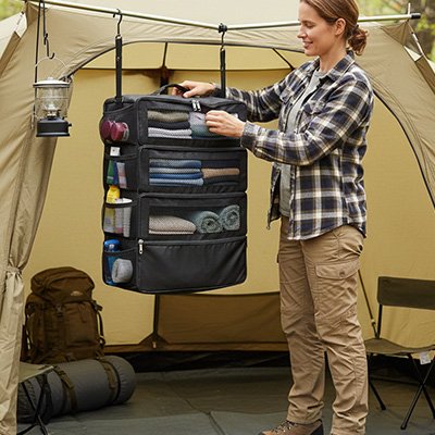 Organisateur de valise suspendu dans une tente de voyage, offrant une solution de rangement compacte et ordonnée pour le camping.