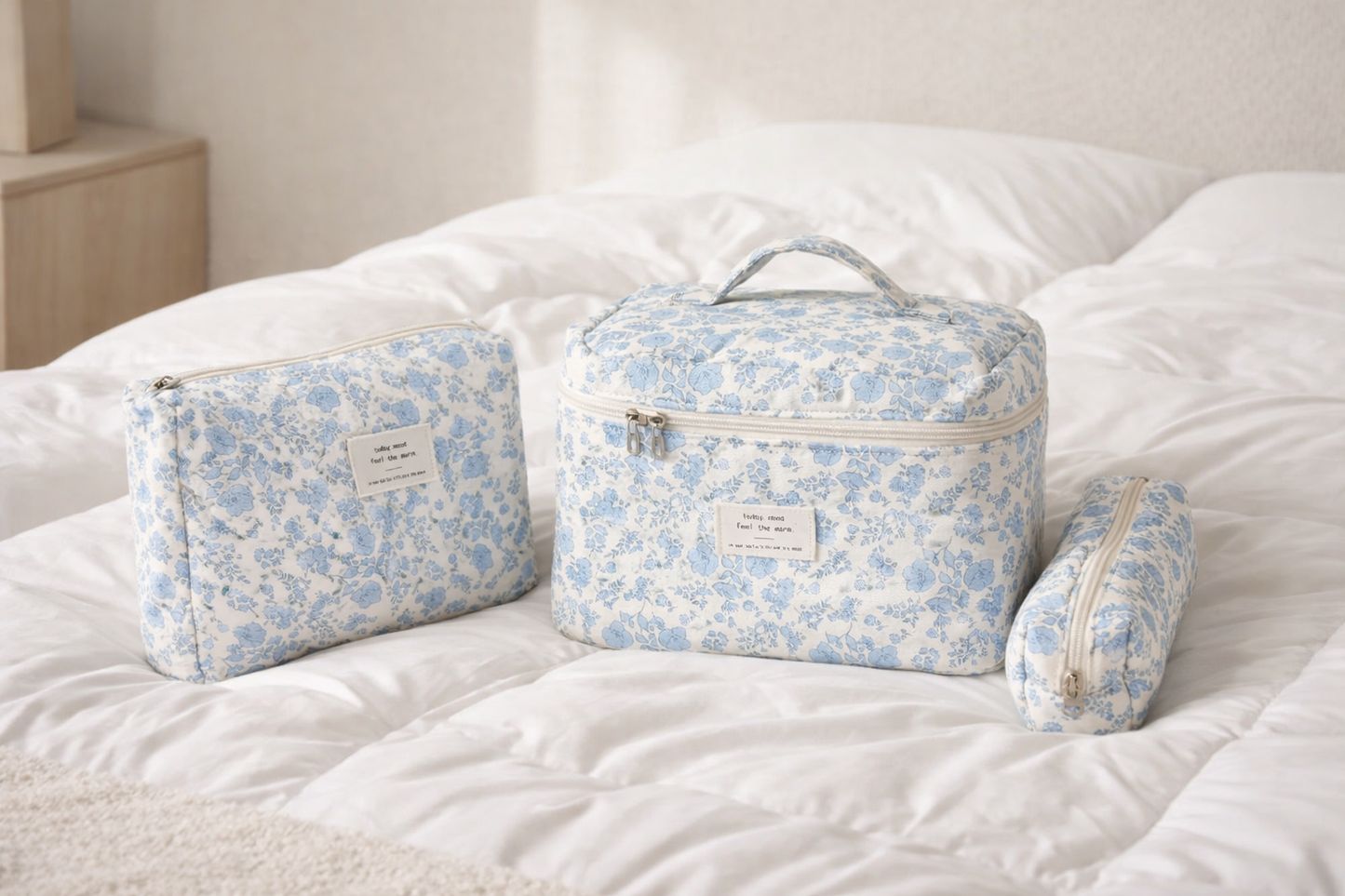 Organisateur de maquillage fleuri, ensemble de trois formats, posé sur lit blanc dans une ambiance zen et voyage