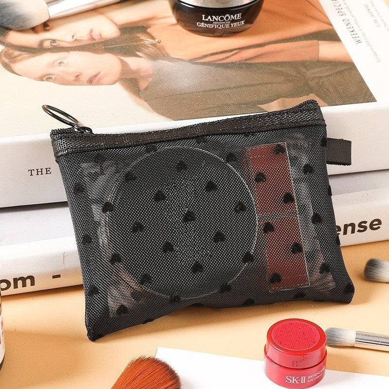 Petite pochette de maquillage noire, posée sur une table de nuit en bois