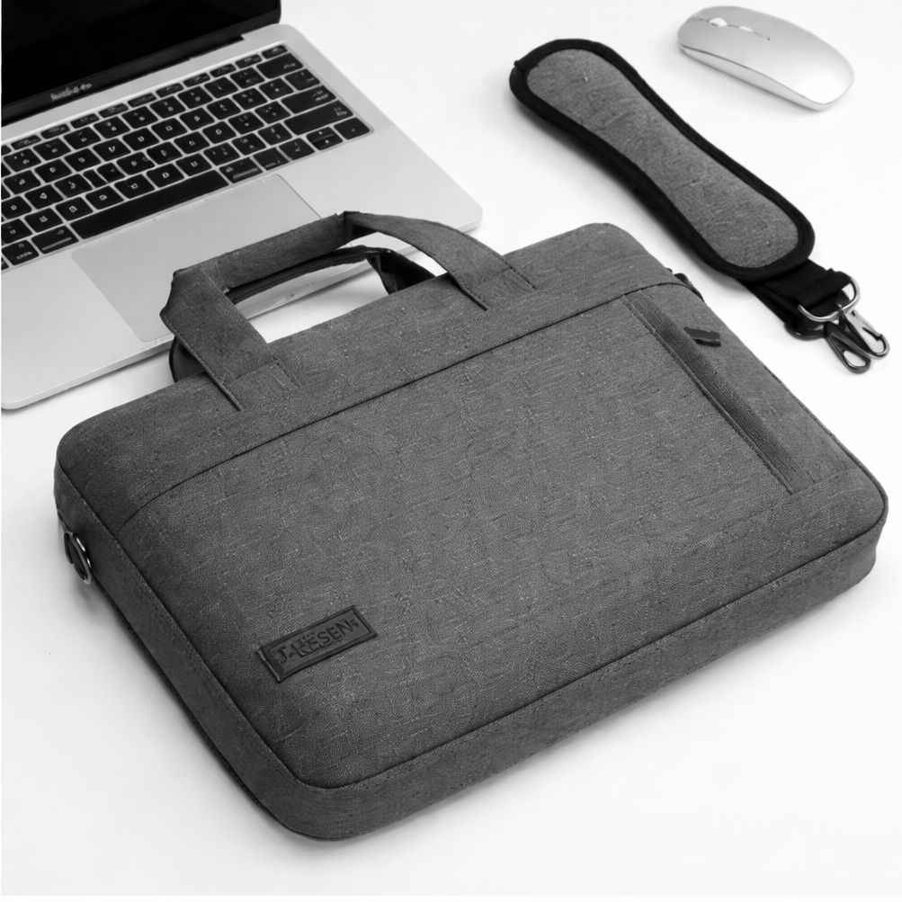 Pochette ordinateur grise avec bandoulière posée près d’un ordinateur et d’une souris.