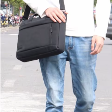 Homme marchant en ville portant une pochette ordinateur noire en bandoulière pour un usage professionnel et quotidien.