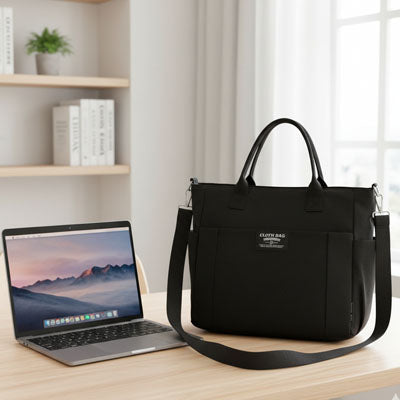 Pochette ordinateur pour femme noire posée sur un bureau à côté d’un ordinateur portable dans un espace de travail moderne et lumineux.