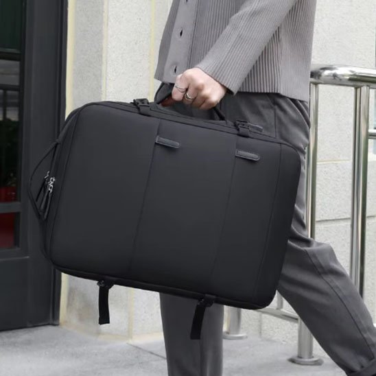Sac à dos de voyage noir porté à la main par un professionnel en tenue élégante, style business urbain en marche vers son bureau