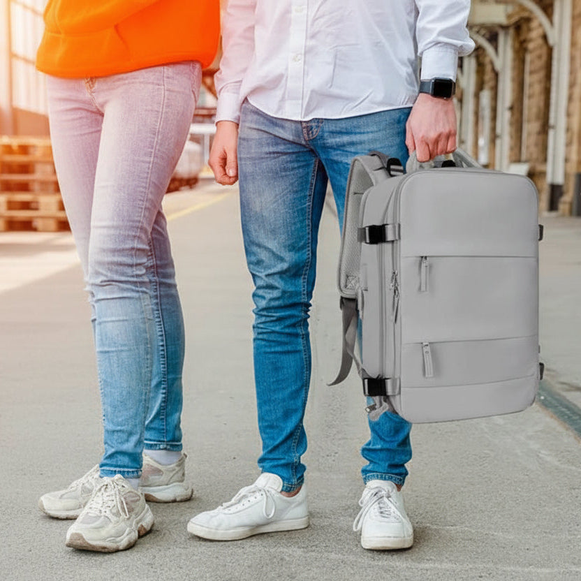 Sac à dos de voyage gris porté à la main par un homme dans un environnement urbain, adapté aux déplacements et aux trajets quotidiens.