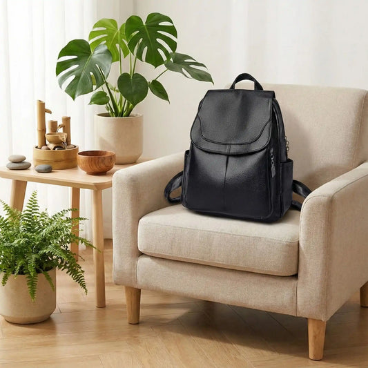 Sac à dos de voyage noir effet cuir grainé posé sur un fauteuil beige, dans un intérieur zen et lumineux avec bois clair et plantes décoratives.