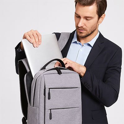Homme en tenue professionnelle glissant un ordinateur portable dans un sac à dos gris, conçu pour protéger et transporter un PC en toute sécurité.