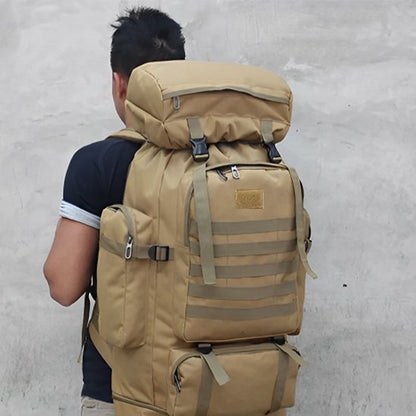 Homme vu de dos portant un grand sac à dos de voyage beige, robuste et volumineux, avec multiples poches et sangles, adapté à la randonnée et aux longs déplacements.