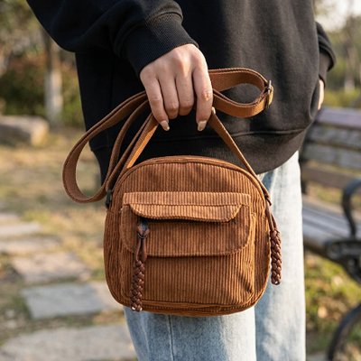 Sac bandoulière femme marron en velours côtelé, porté à la main en extérieur