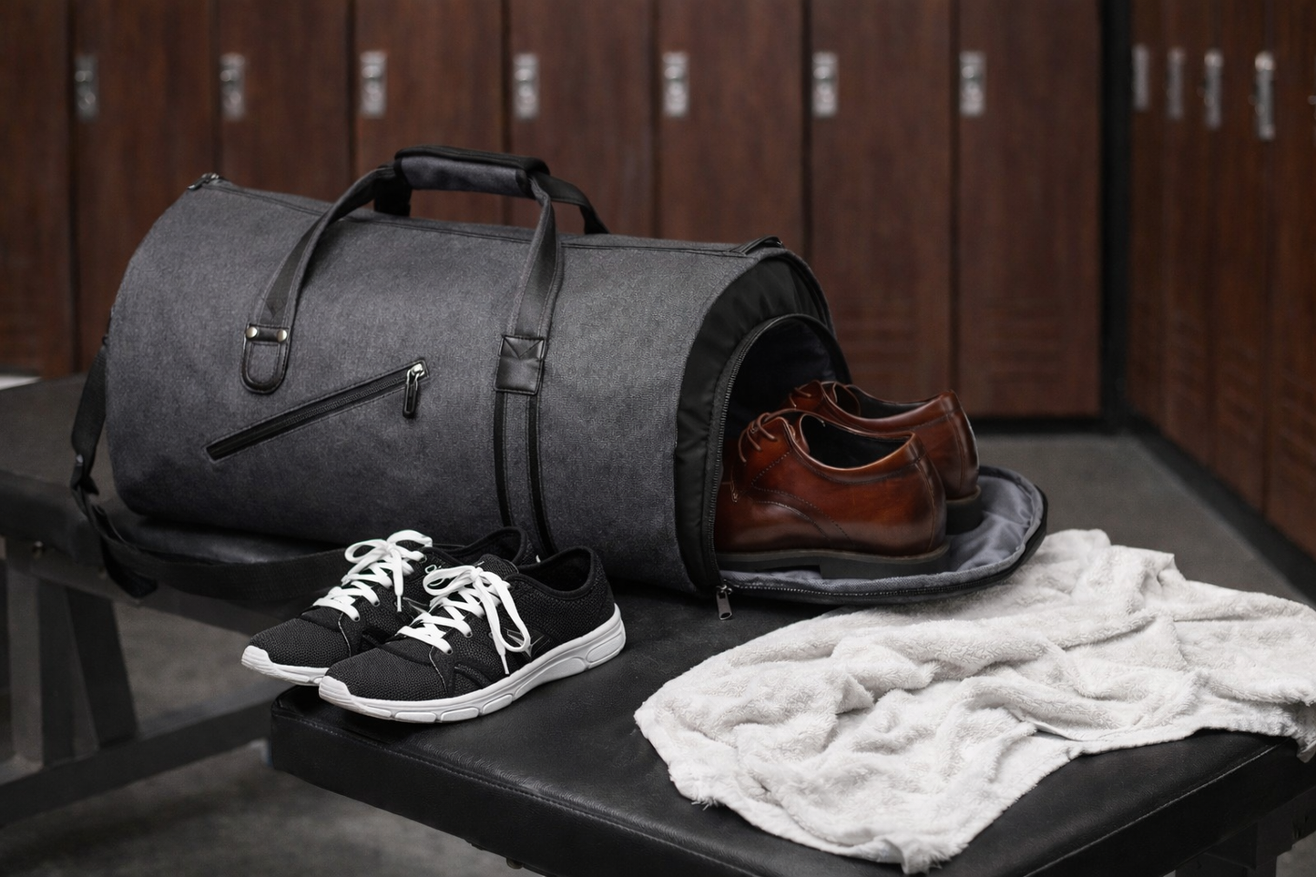sac de sport gris noir pose sur banc de salle de sport avec compartiment chaussures ouvert contenant chaussures paire de baskets noir et blanc a cote serviette humide sur banc casier