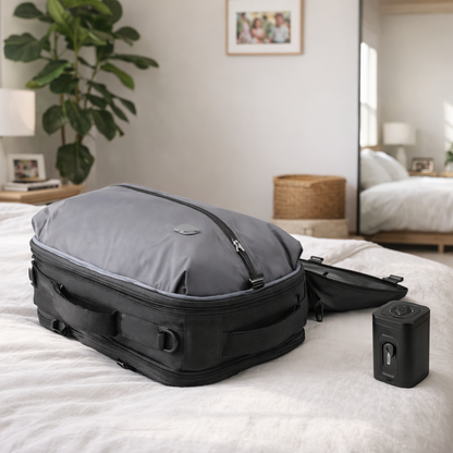 Sac de voyage à dos gris et noir posé sur fond blanc, montrant un design compact et structuré, accompagné d’un accessoire de compression pour optimiser le rangement sur un lit