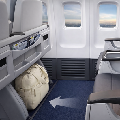 Sac de voyage femme beige rangé sous un siège d’avion, format cabine compact, idéal pour transporter les essentiels lors d’un vol confortable seule ou en famille.