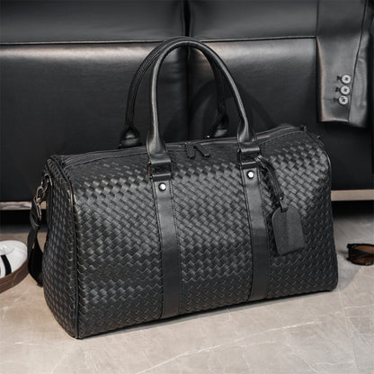 Sac de voyage noir effet cuir haute gamme posé au sol devant un canapé en cuir noir, ambiance intérieur d'un bureau moderne