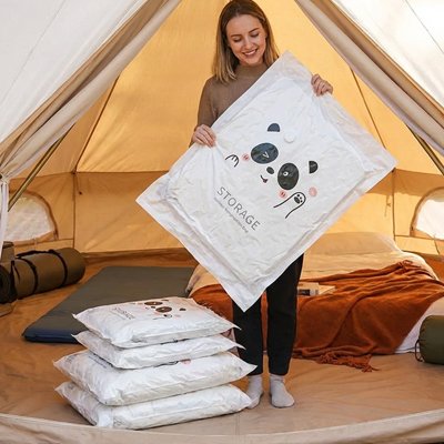 Sac sous vide optimisant le voyage, femme souriante tenant grand sac blanc, pile de sacs compressés dans tente beige chaleureuse prêt à partir léger