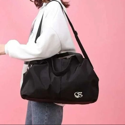 Sac week end femme noir élégant porté à l’épaule, femme marchant près d’un mur rose