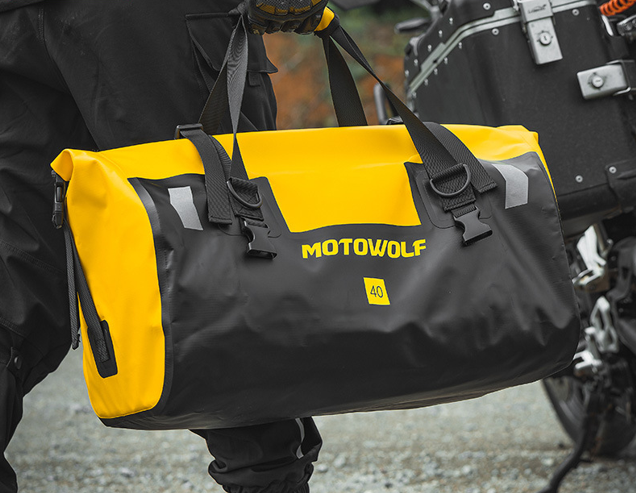 Sac week-end homme jaune transporté par les poignées par un homme descendant de sa moto