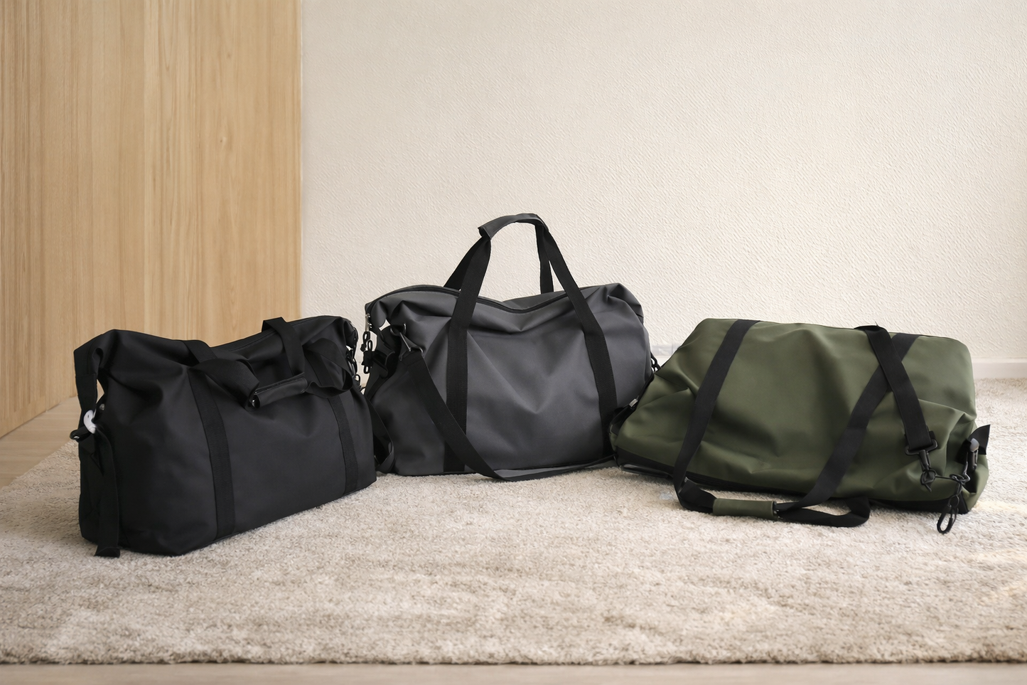 Sac week end noir gris et vert posés au sol dans une ambiance zen et minimaliste en intérieur. Les sacs sont présentés côte à côte sur un tapis clair.