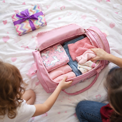 Sac Week End Zen Girly Aventure rose ouvert sur un lit, contenant des vêtements d’enfant dans une ambiance douce et zen.