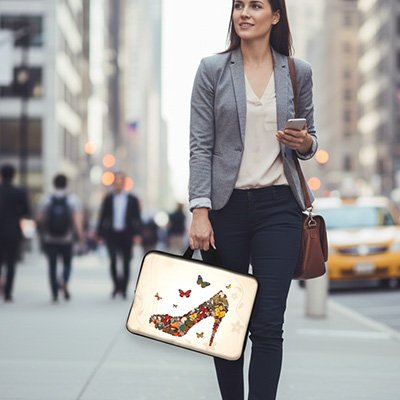 Sacoche ordinateur femme élégante avec illustration artistique de chaussure à talon et papillons, portée à la main lors d’un déplacement urbain