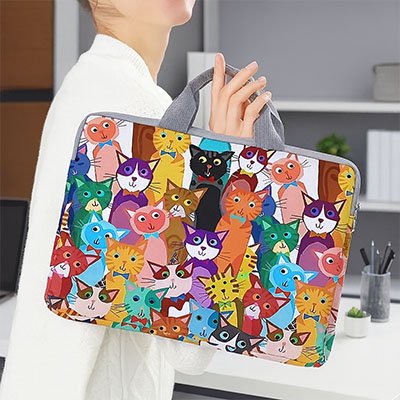 Sacoche pour ordinateur colorée à motifs de chats, portée à la main par une personne debout dans un bureau moderne.