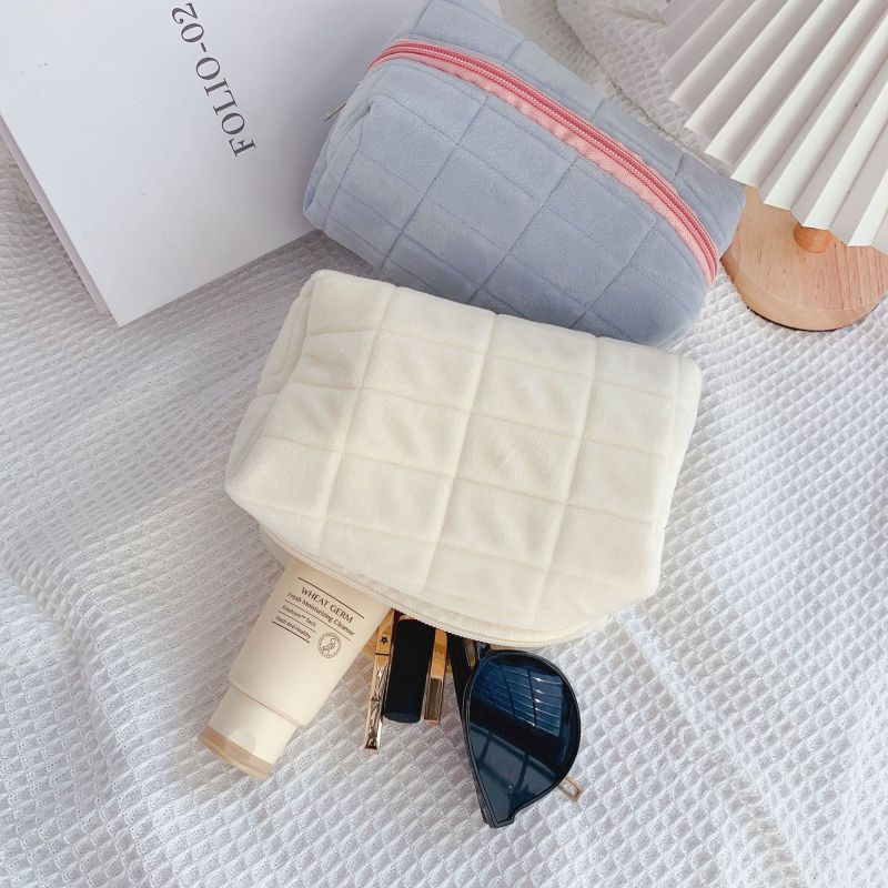 trousse à maquillage velours matelassé bleu ciel et blanc crème minimaliste sur fond texturé avec accessoires beauté
