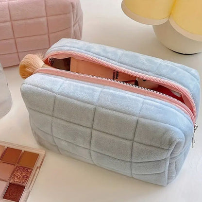 trousse à maquillage velours matelassé bleu posée sur table blanche fermeture éclair rose