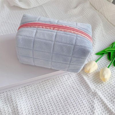 trousse à maquillage velours matelassé bleu posée sur table blanche style minimaliste