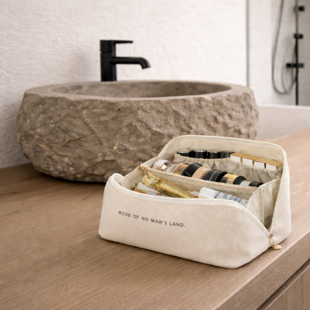 Trousse cosmétique beige sur comptoir bois clair salle de bain hôtel avec évier pierre et douche italienne noir blanc