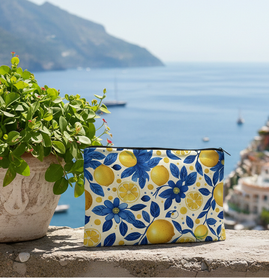 trousse de maquillage fantaisie motif citrons jaunes et fleurs bleues posée sur muret en pierre avec vue mer et village côtier