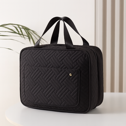 Trousse de toilette femme rétro noire, posée sur une table blanche, design matelassé élégant, style intemporel et raffiné.